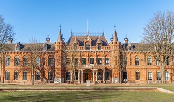 Un edificio grande e histórico con fachada simétrica, ventanas arqueadas y una entrada central.