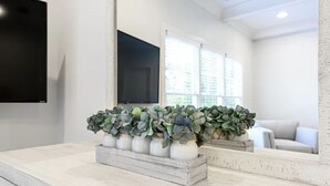A modern living room with a white fireplace, a mounted flat-screen TV, and a large window with blinds.