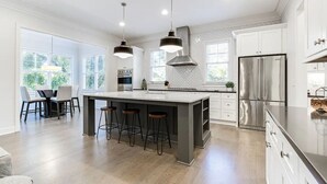 A modern kitchen with a central island, bar stools, stainless steel appliances, and large windows.