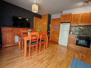 A kitchen with wooden cabinets, a dining table with chairs, a refrigerator, and an oven.
