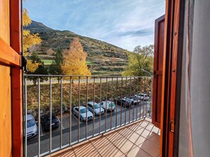 A balcony with a view of parked cars and a hilly landscape.