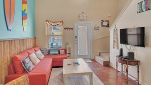 Ein Wohnzimmer mit rotem Sofa, weißem Couchtisch, Fernseher auf einem Holzständer und einem großen Fenster mit Jalousien.