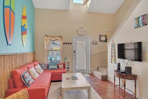 A living room with a red sofa, a white coffee table, a TV on a wooden stand, and a large window with blinds.