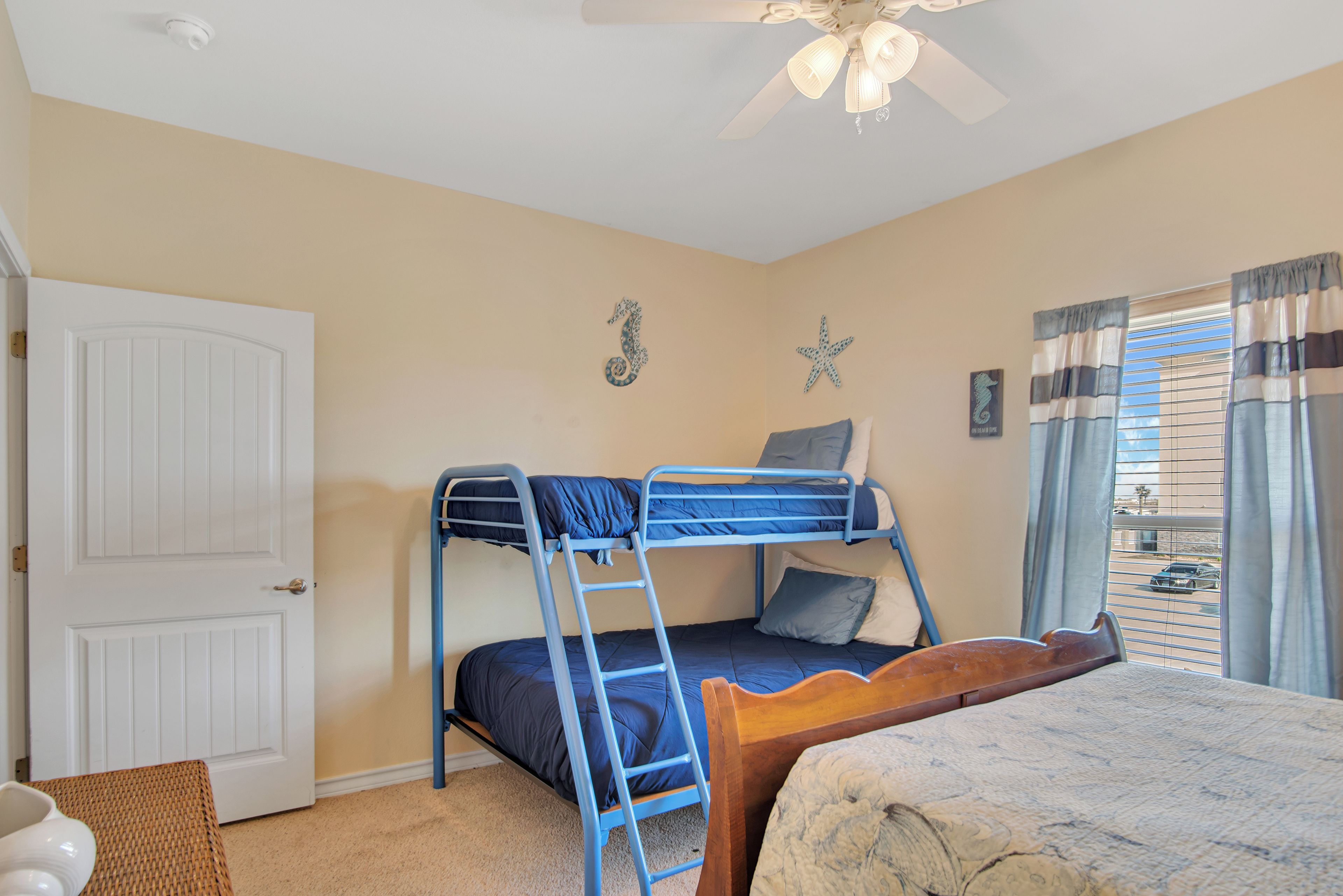 A bedroom with a bunk bed, a wooden headboard, a ceiling fan, and a window with curtains.
