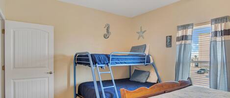 A bedroom with a bunk bed, a wooden headboard, a ceiling fan, and a window with curtains.