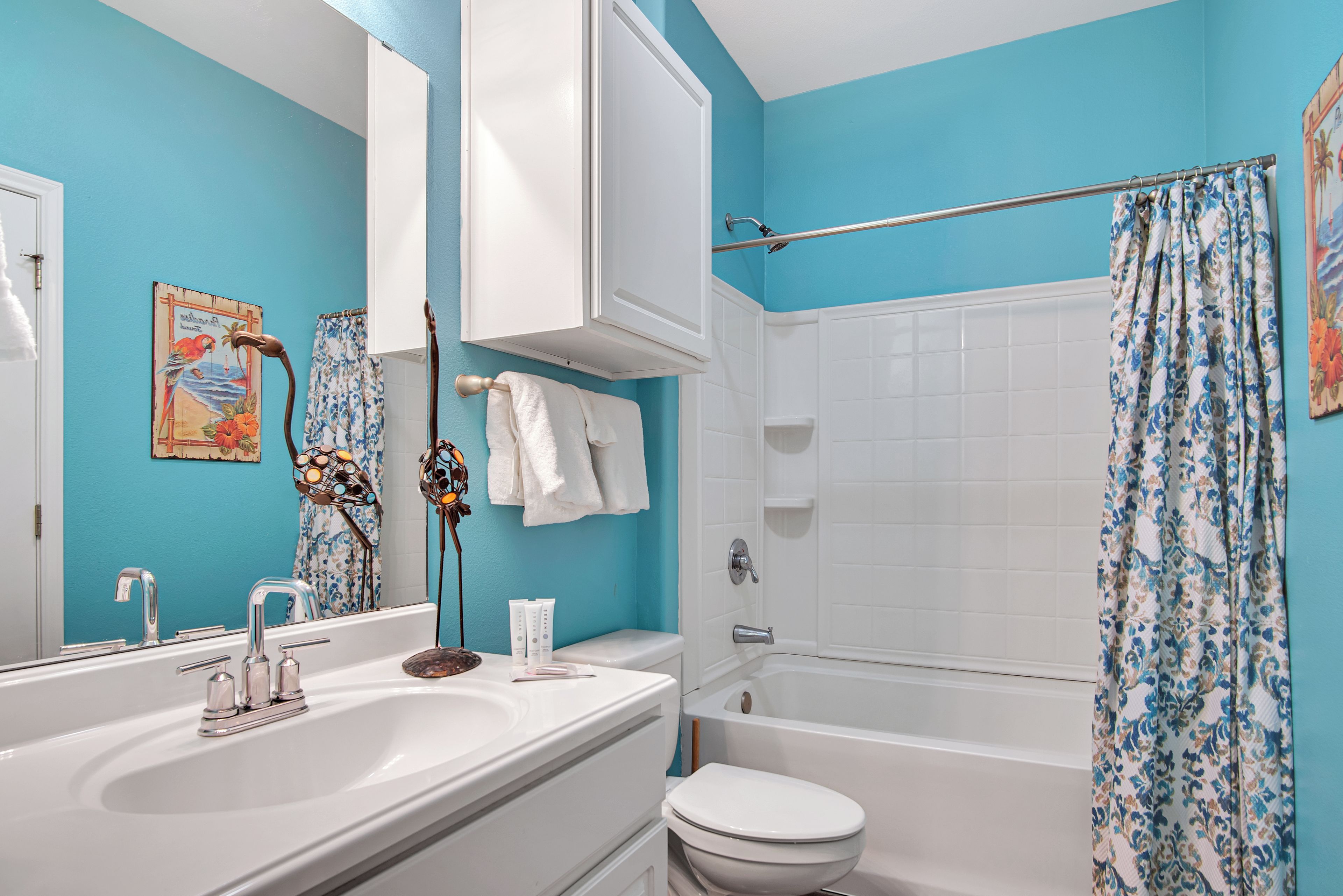 A bathroom with a blue wall, white fixtures, a bathtub, and a shower curtain.