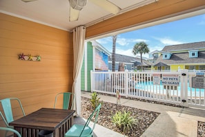 A patio with a wooden table and chairs, a white fence, and a pool with signs indicating no pets and no glass. - Happiness Comes In Waves by Silver Sands Vacation Rentals (Port Aransas)