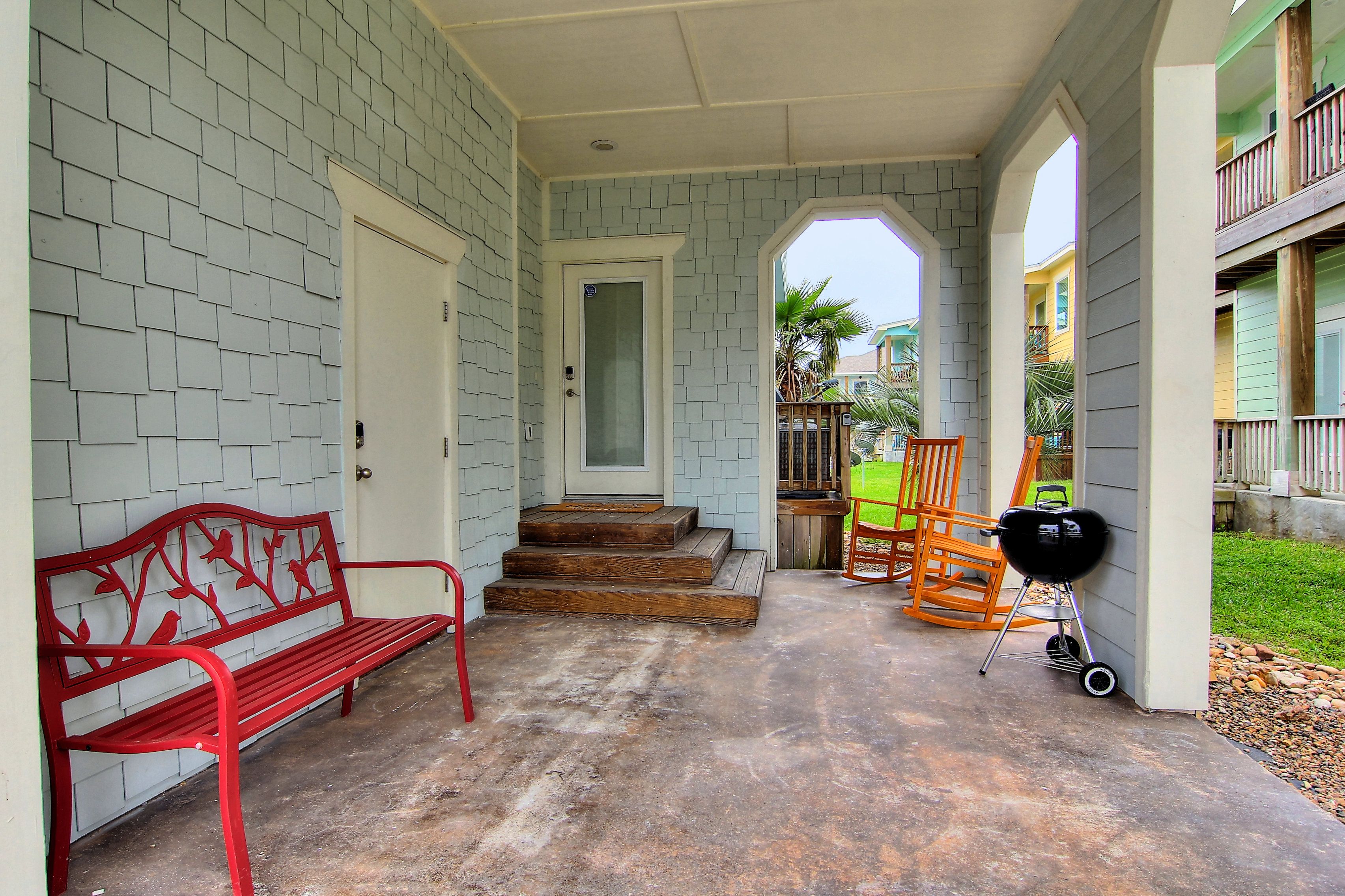 A covered porch with a red bench, a wooden bench, and a grill.