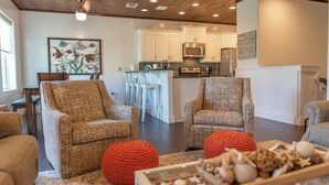 A modern living room with two patterned armchairs, a coffee table with decorative items, and a kitchen area in the background. - Getaway by Silver Sands Vacation Rentals (Port Aransas)