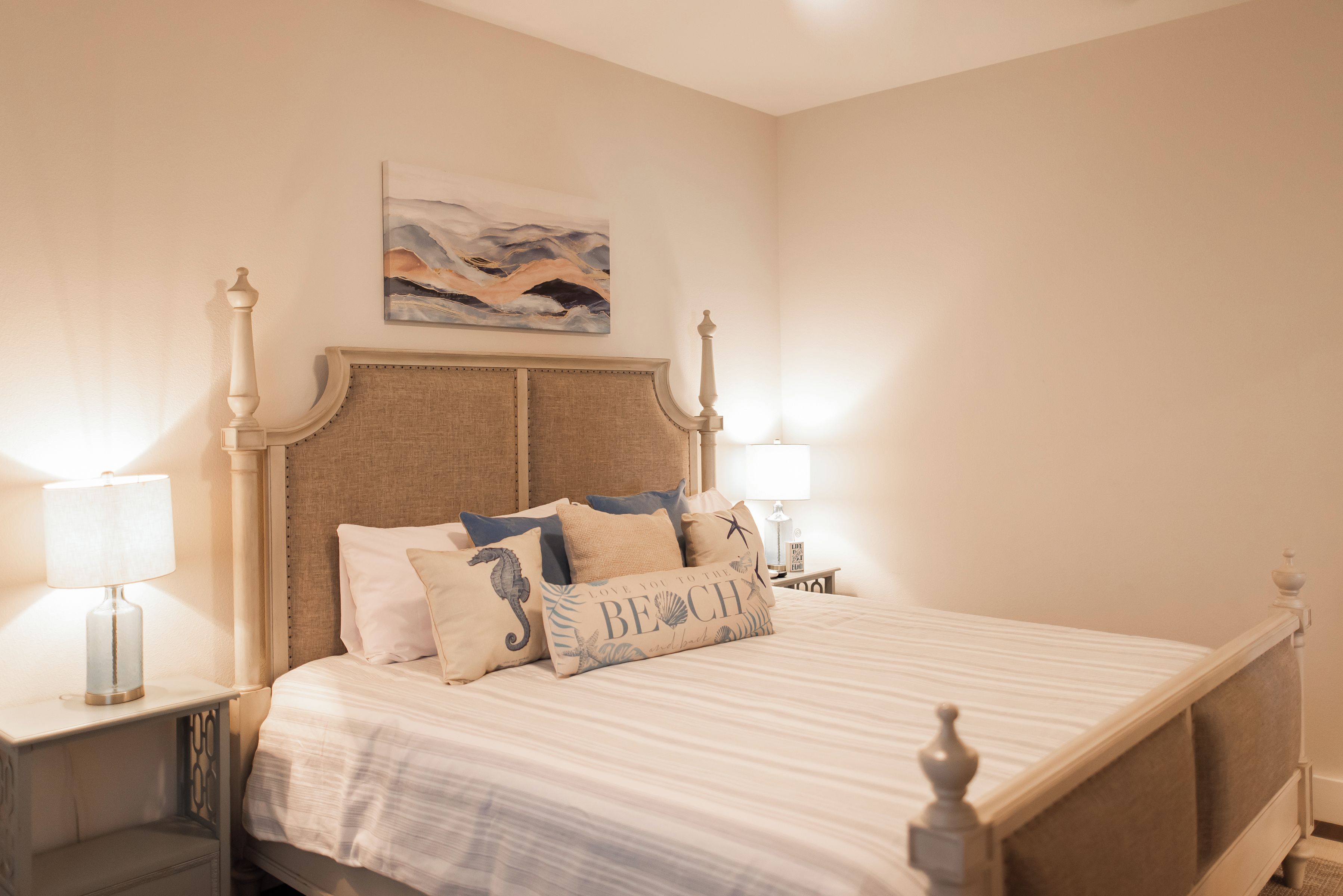 A neatly made bed with a striped bedspread and decorative pillows, a headboard with a decorative design, and a painting above the bed.