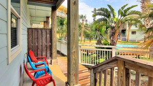 A wooden deck with a pool, surrounded by palm trees and a building with a balcony. - Getaway by Silver Sands Vacation Rentals (Port Aransas)