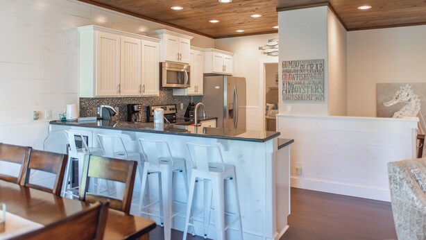 A modern kitchen with white cabinets, stainless steel appliances, and a bar area with stools. - Getaway by Silver Sands Vacation Rentals (Port Aransas)