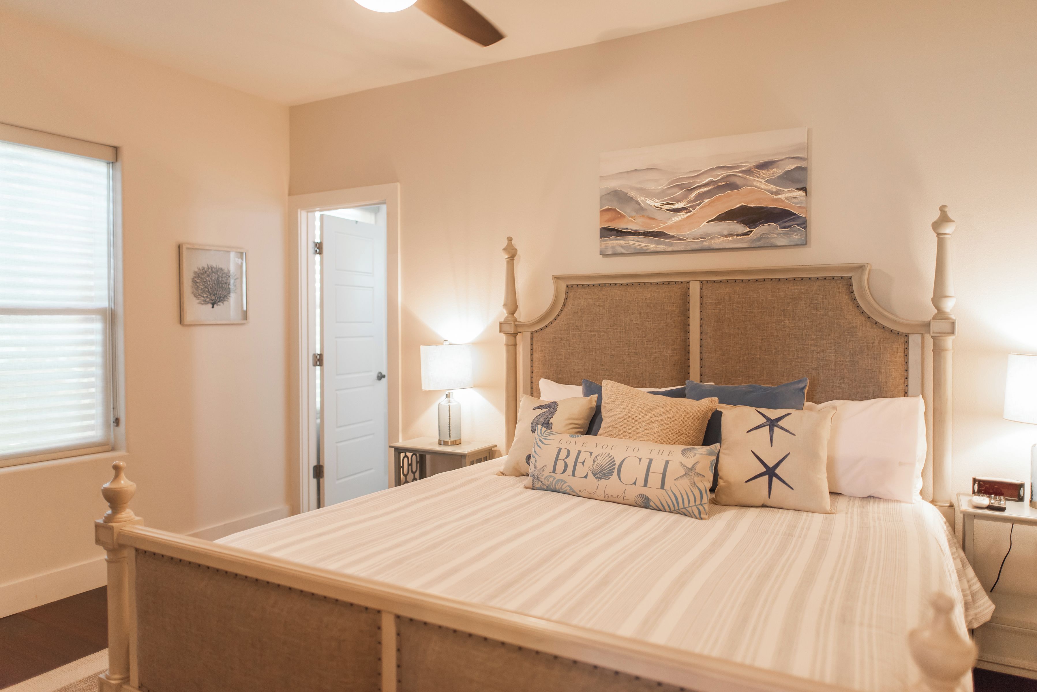 Una camera da letto con un letto, un comodino, una lampada, una porta e un quadro appeso al muro.