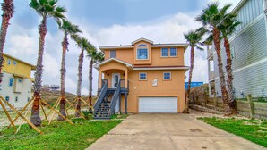 A two-story house with a front garage, palm trees, and a concrete driveway. - Happy Heron by Silver Sands Vacation Rentals (Port Aransas)