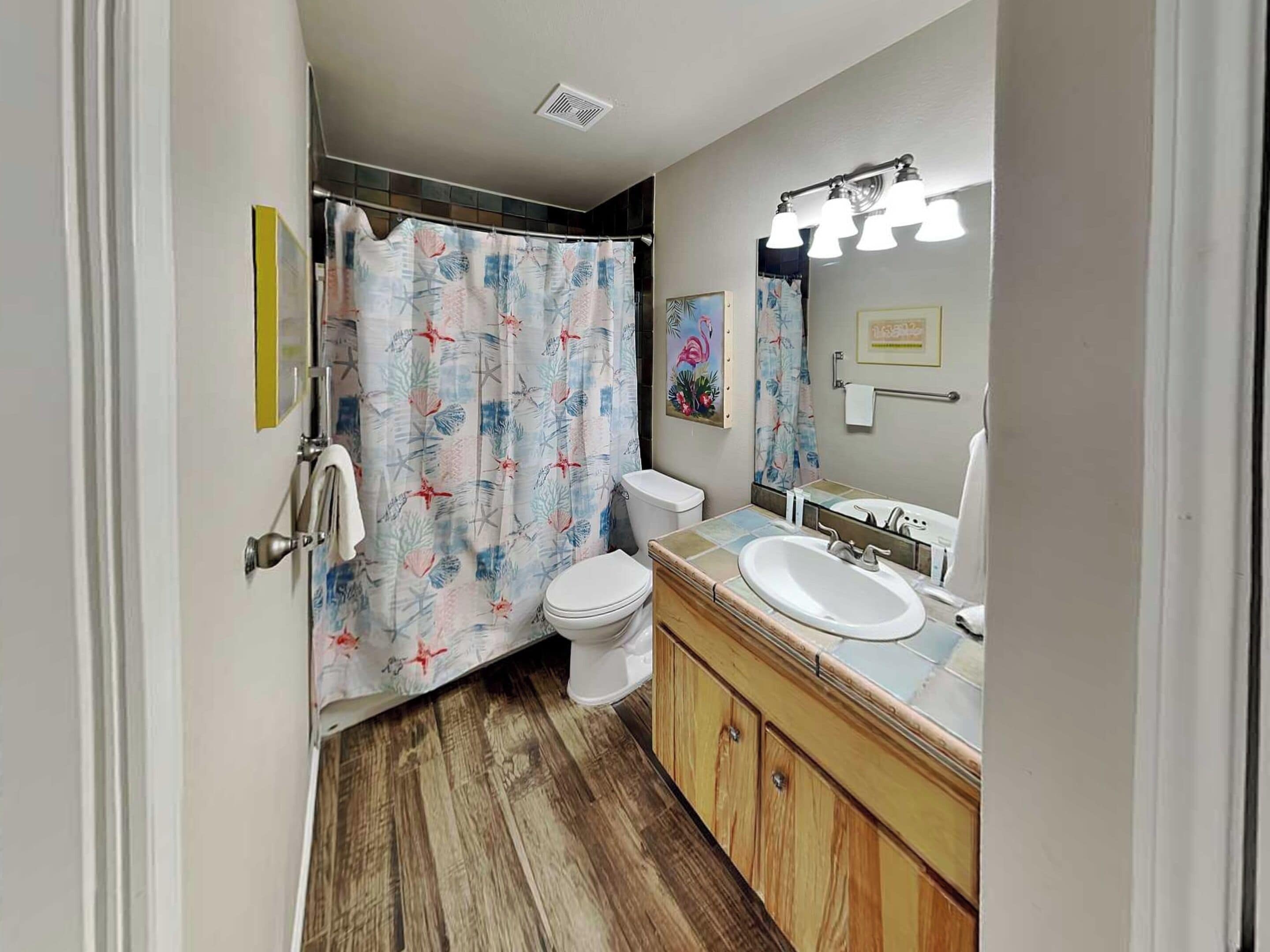A bathroom with a shower curtain, toilet, sink, and vanity.