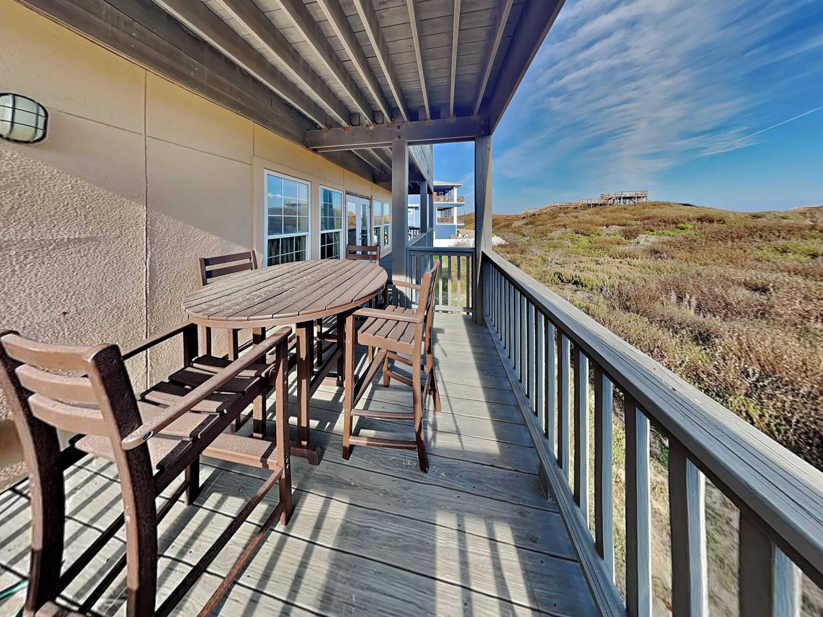 A covered outdoor deck with a wooden table and chairs, overlooking a hilly landscape.