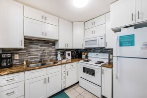 A modern kitchen with white cabinets, a granite countertop, a built-in microwave, a stove, and a refrigerator.