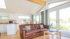 A modern living room with a brown leather sofa, a wooden coffee table, and a kitchen area with white cabinets and a microwave. - 5 Meadow Retreat (Liskeard)