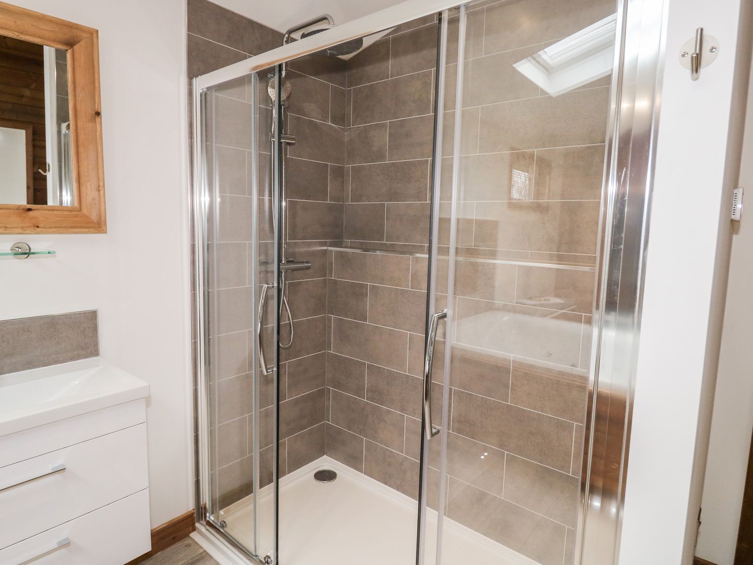 Una cabina doccia con pareti in vetro, un lavandino bianco e uno specchio con cornice in legno.