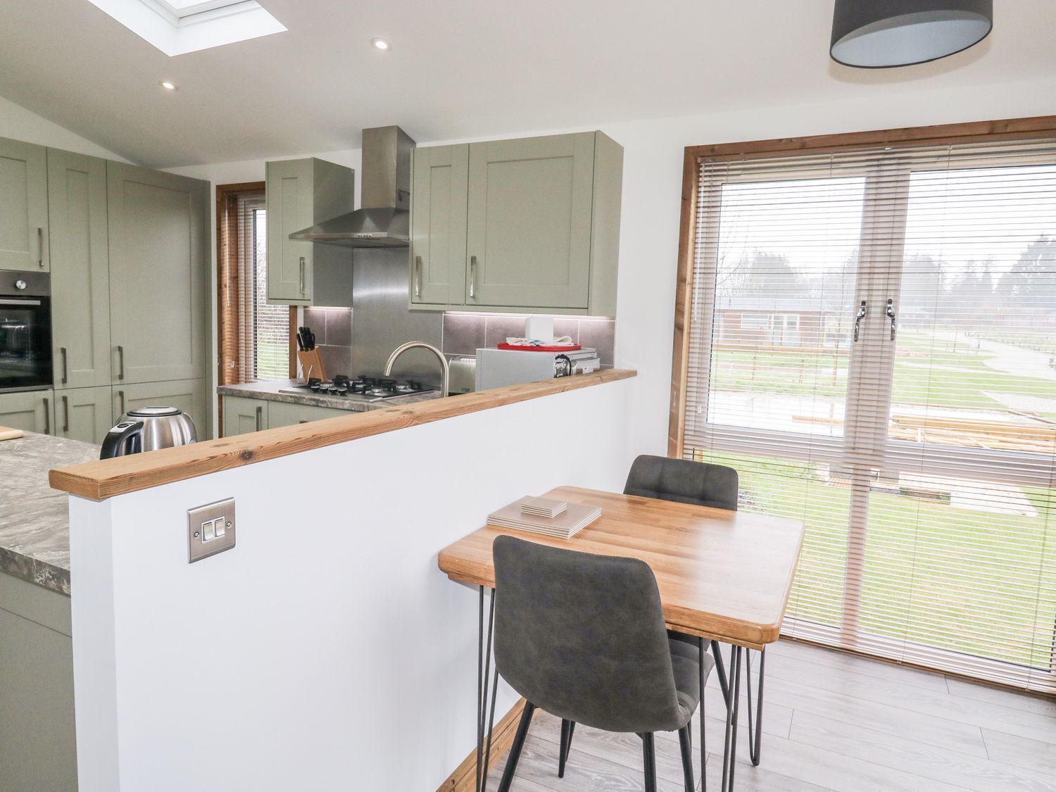 A modern kitchen with a central island, a dining area with a table and chairs, and a large sliding glass door leading to a view of a green landscape.