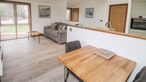 A modern kitchen with a wooden countertop, a dining table, and a sofa in a spacious living area with large windows. - 2 Meadow Retreat (Liskeard)
