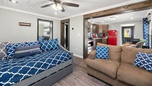 A modern living room with a sofa and a couch, a ceiling fan, and a kitchen area visible through an open doorway. - Sharpe Tiny House — Cozy, Remodeled Home with Big Amenities (Statesville)