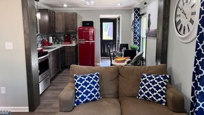 A modern living room with a brown sofa, two patterned cushions, a red refrigerator, and a large wall clock. - Sharpe Tiny House — Cozy, Remodeled Home with Big Amenities (Statesville)