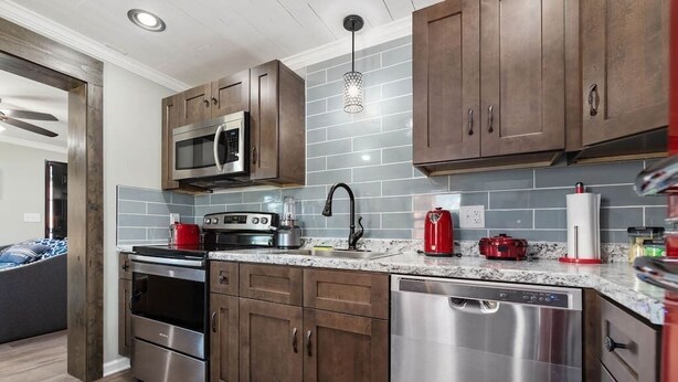 A modern kitchen with dark wooden cabinets, stainless steel appliances, and a tiled backsplash. - Sharpe Tiny House — Cozy, Remodeled Home with Big Amenities (Statesville)