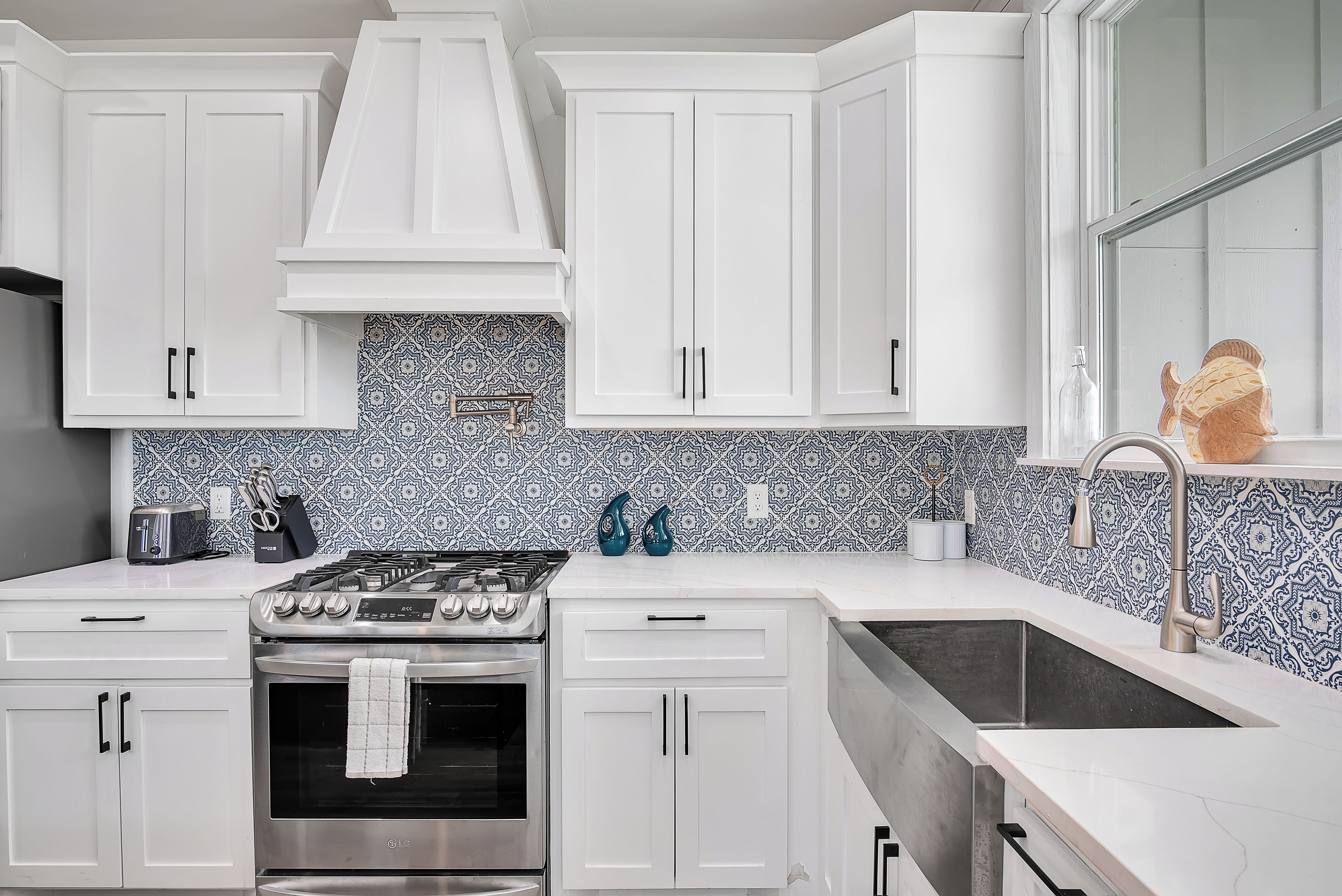 A kitchen with white cabinets, a stainless steel stove, and a patterned backsplash.