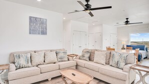 Un salon avec un canapé d’angle beige, une table basse en bois et un ventilateur de plafond.