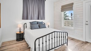 Une chambre à coucher avec un lit, deux tables de chevet avec des lampes, une fenêtre donnant sur un beau paysage et un ventilateur de plafond.