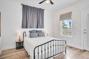 A bedroom with a bed, two bedside tables with lamps, a window with a view, and a ceiling fan. - Holy Moly by Silver Sands Vacation Rentals (Port Aransas)