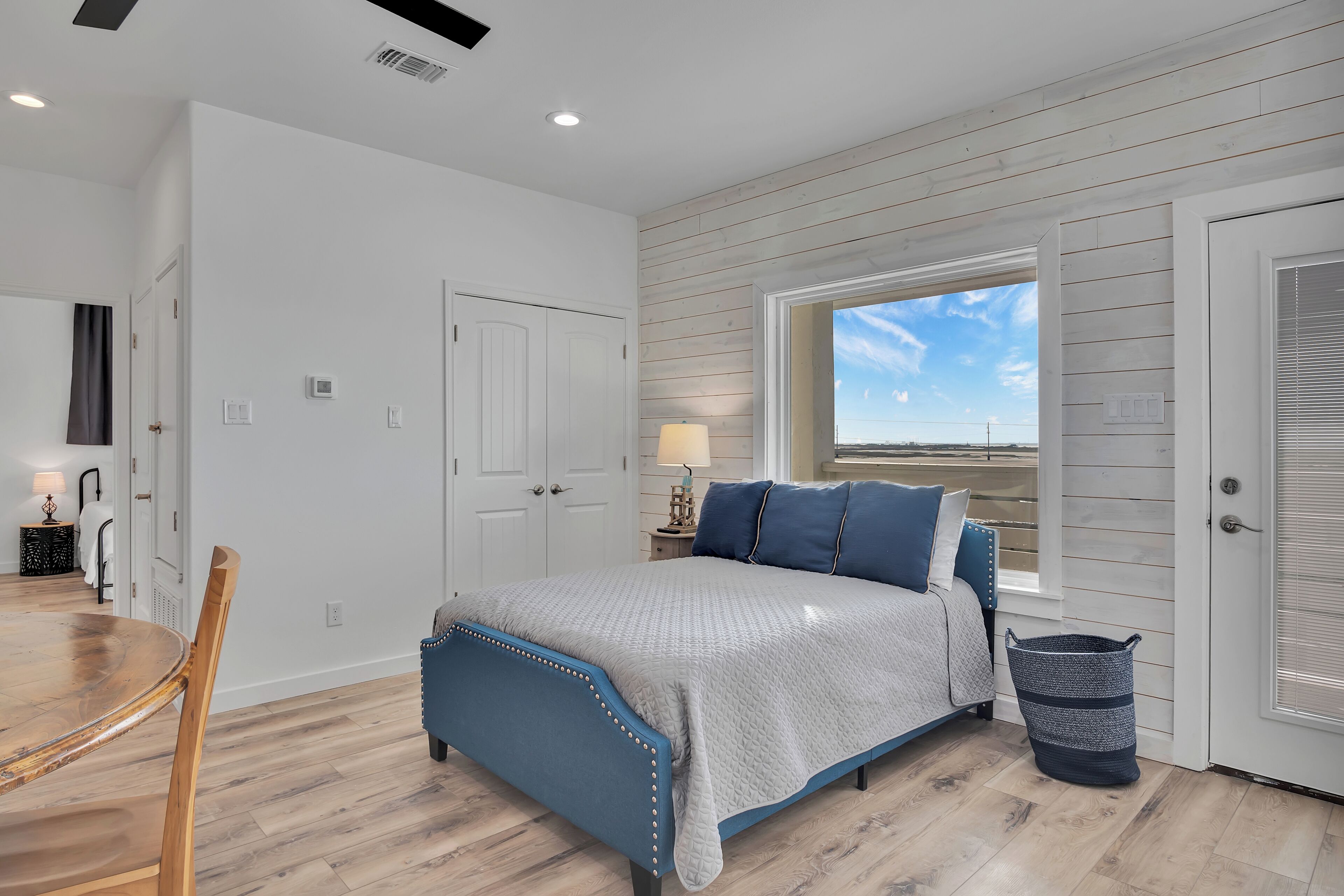 A bedroom with a bed, a window, a lamp, and a trash can.