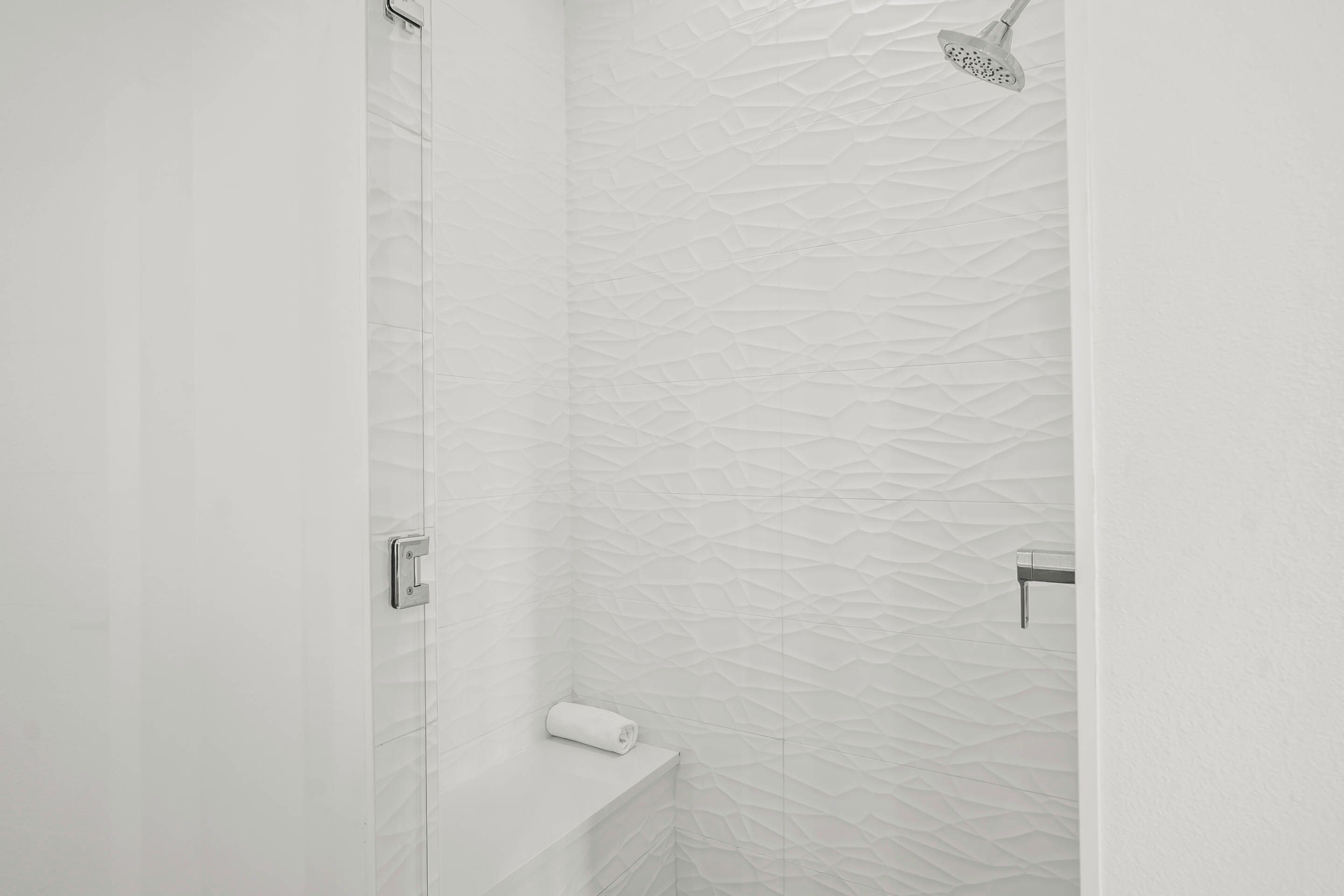 A modern bathroom with a textured wall, a showerhead, and a towel rack.