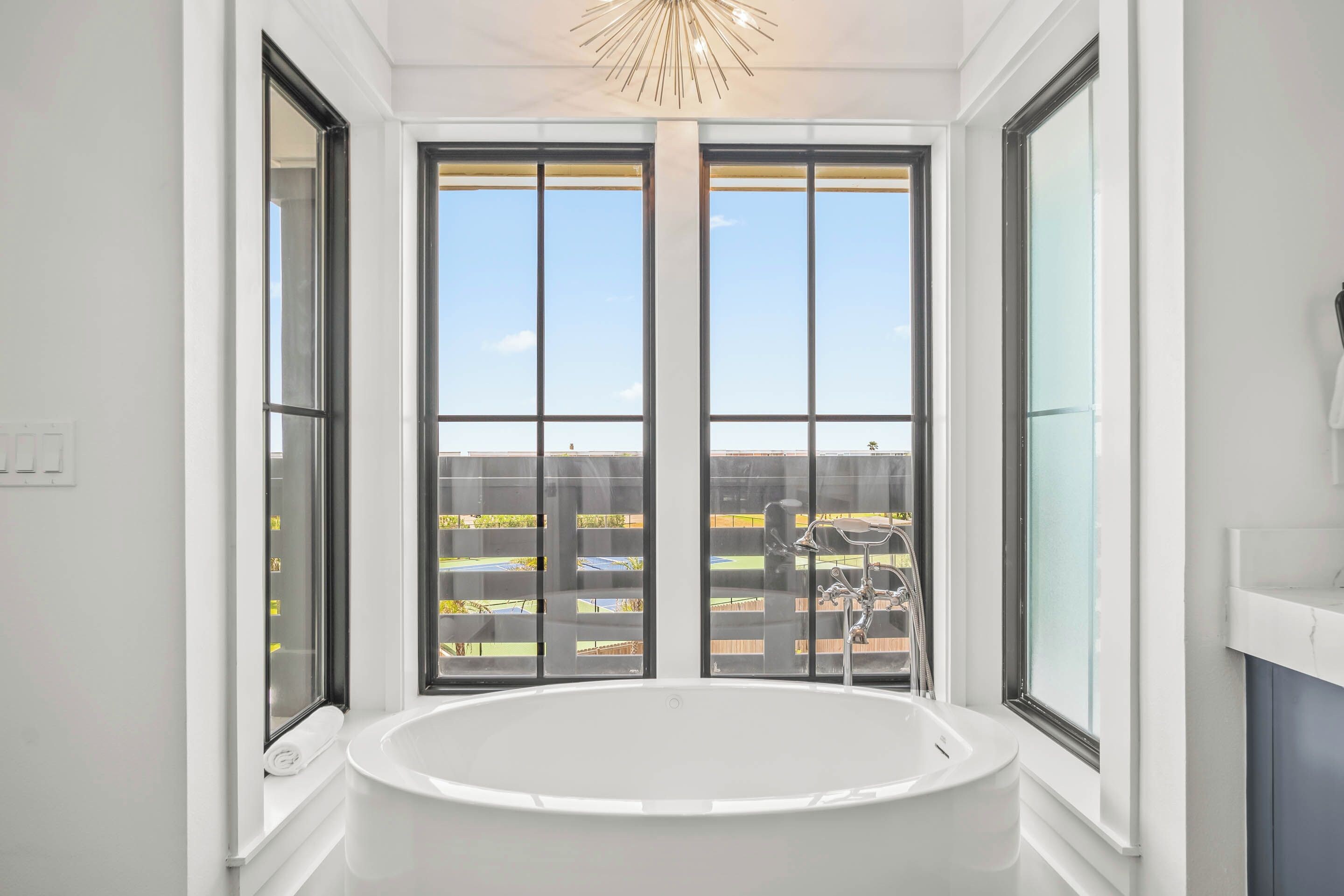 Ein Badezimmer mit einer großen Badewanne, zwei Fenstern und Blick auf einen umzäunten Außenbereich.