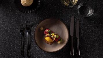 A dark, textured table with a plate of food, a glass of water, and cutlery.