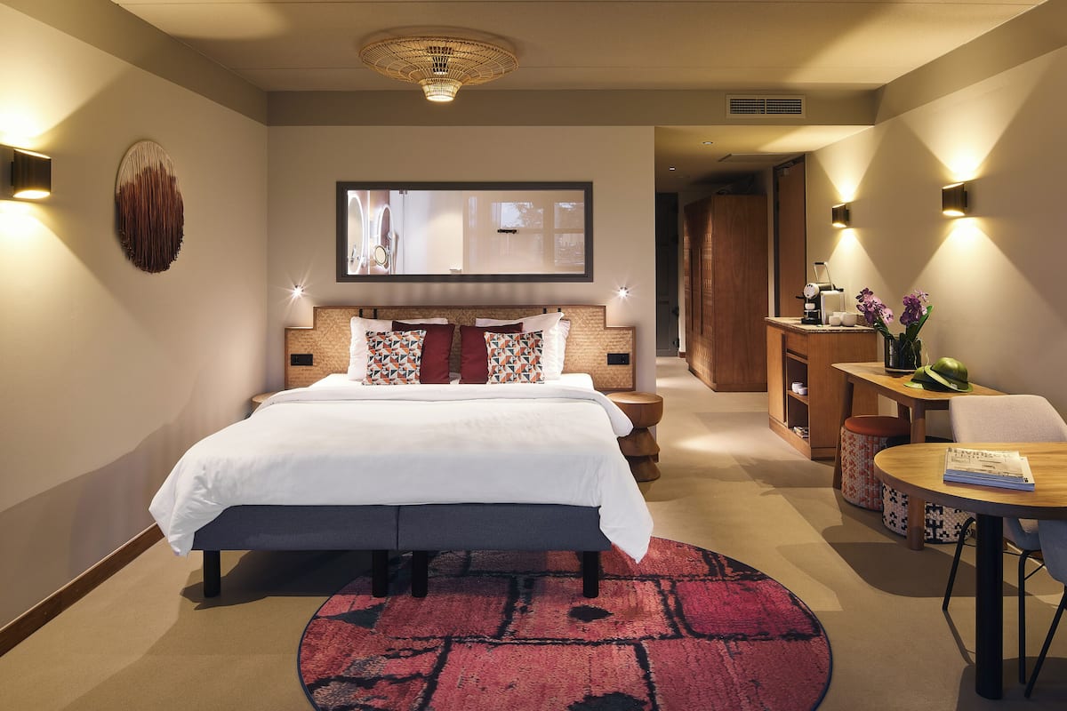 A modern hotel room with a large bed, a round rug, a small table with a book, and a desk with a chair.