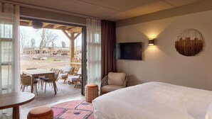 A hotel room with a bed, a TV, a dining area with chairs and a table, and a view of the outdoor area. - Safari Hotel Beekse Bergen (Hilvarenbeek)