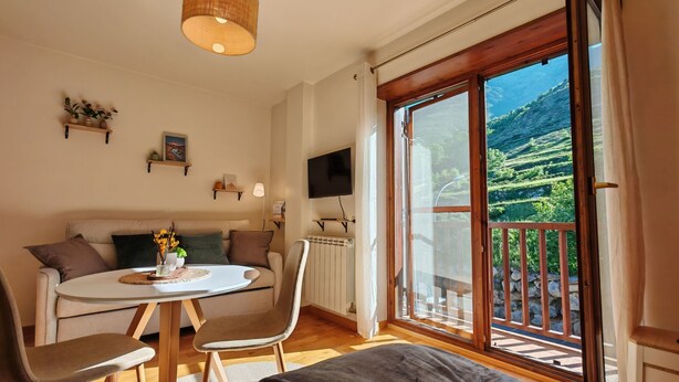Une pièce confortable avec un lit, une table ronde entourée de chaises, un canapé, un téléviseur et une grande fenêtre donnant sur des collines verdoyantes.