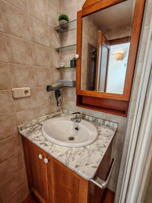 Une salle de bain avec un lavabo en marbre, des meubles en bois, un miroir et une petite étagère sur laquelle est posée une plante.