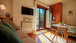 Un salon comprenant un canapé, une table avec des chaises, un téléviseur fixé au mur et une fenêtre donnant sur un paysage verdoyant.