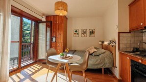 Une pièce confortable comprenant une table à manger, des chaises, un lit, un coin cuisine et une porte-fenêtre coulissante donnant sur un balcon.