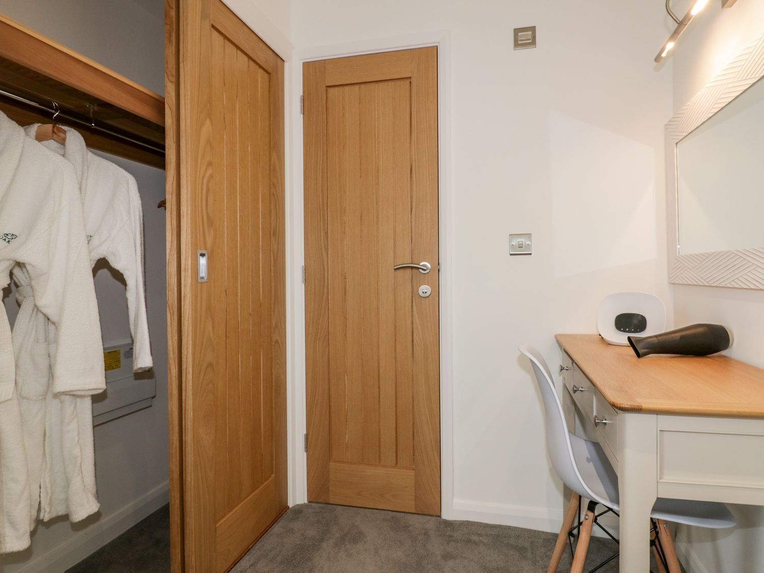 A bathroom with a wooden door, a white towel rack with towels, a white chair, a vanity with a mirror, and a hairdryer on the counter.