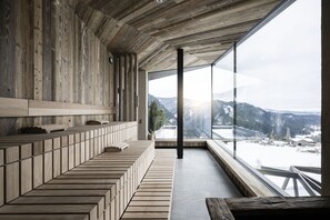 A modern interior with a wooden bench seating area, large windows offering a view of a snowy landscape. - Aparthotel My Daum (Nova Ponente)