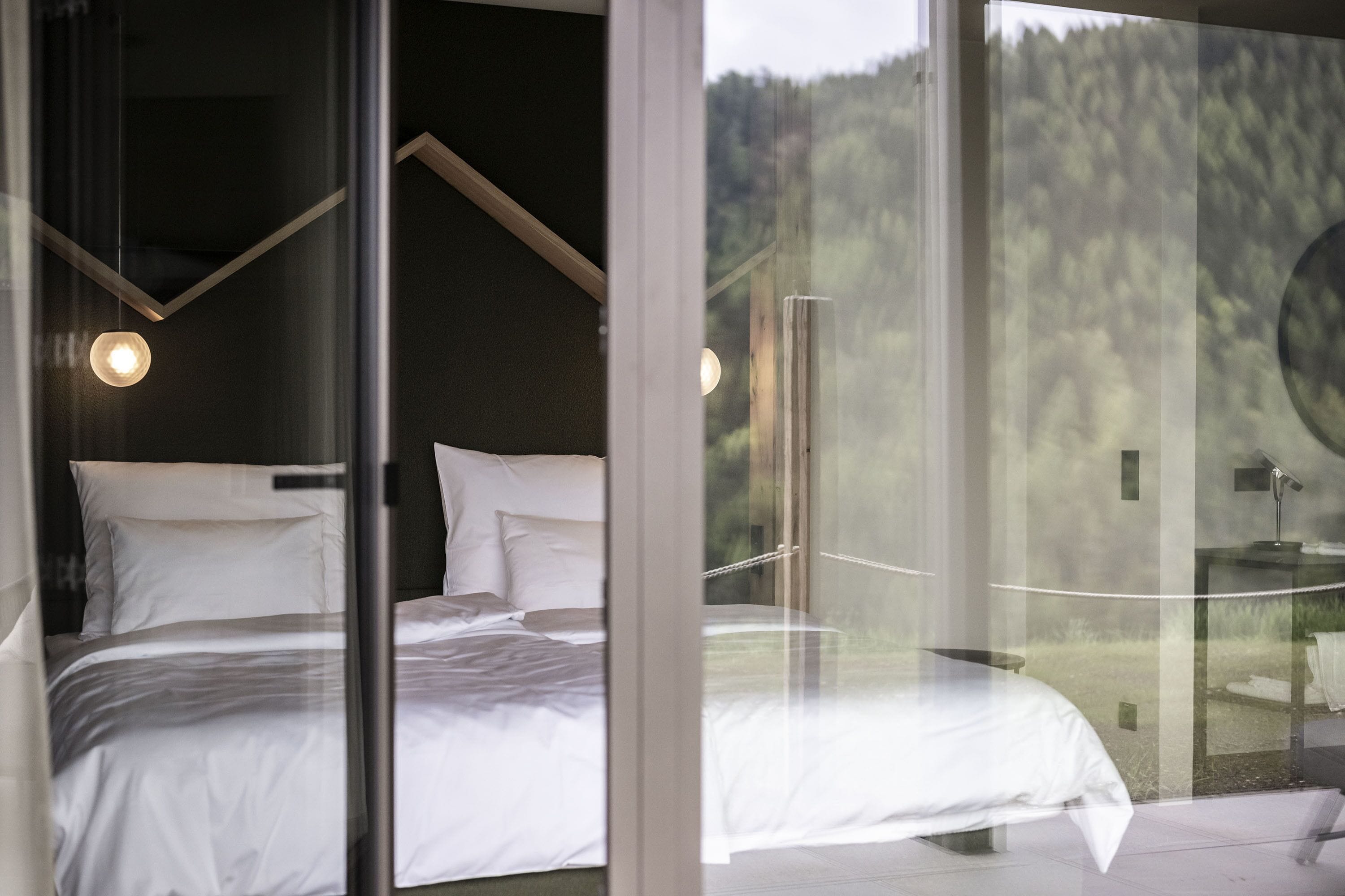 Una camera da letto con un letto, una parete di vetro e vista su una foresta.