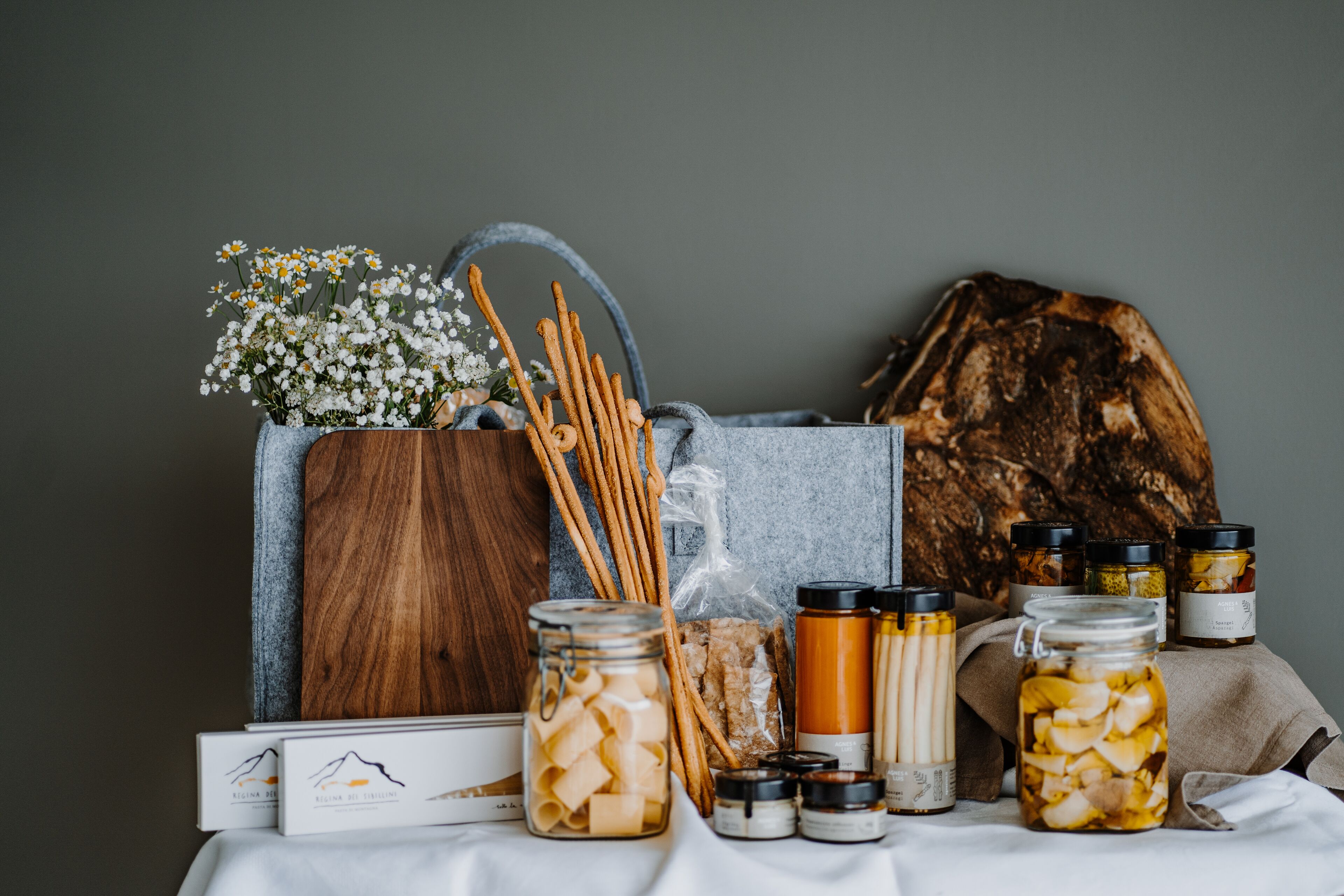 Una mesa con frascos de verduras encurtidas, una cesta de madera con flores y un fondo rústico.