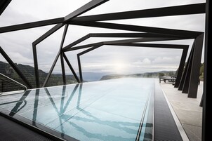 A glass-enclosed infinity pool with a view of a mountainous landscape.