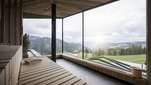 Een houten terras met uitzicht op een bergachtig landschap door grote ramen.