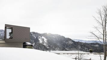 Un edificio moderno con un diseño geométrico único, un balcón con vistas a montañas nevadas y un cielo despejado.