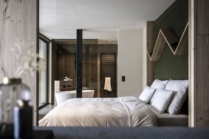 A modern bedroom with a large bed, a glass shower enclosure, and a view of the outdoors.